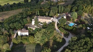 An aerial view of a rural estate with a large stone building, a swimming pool, and surrounding greenery.