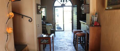 A narrow stone-floored hallway with a wooden table and chairs, a staircase, and a door leading outside.