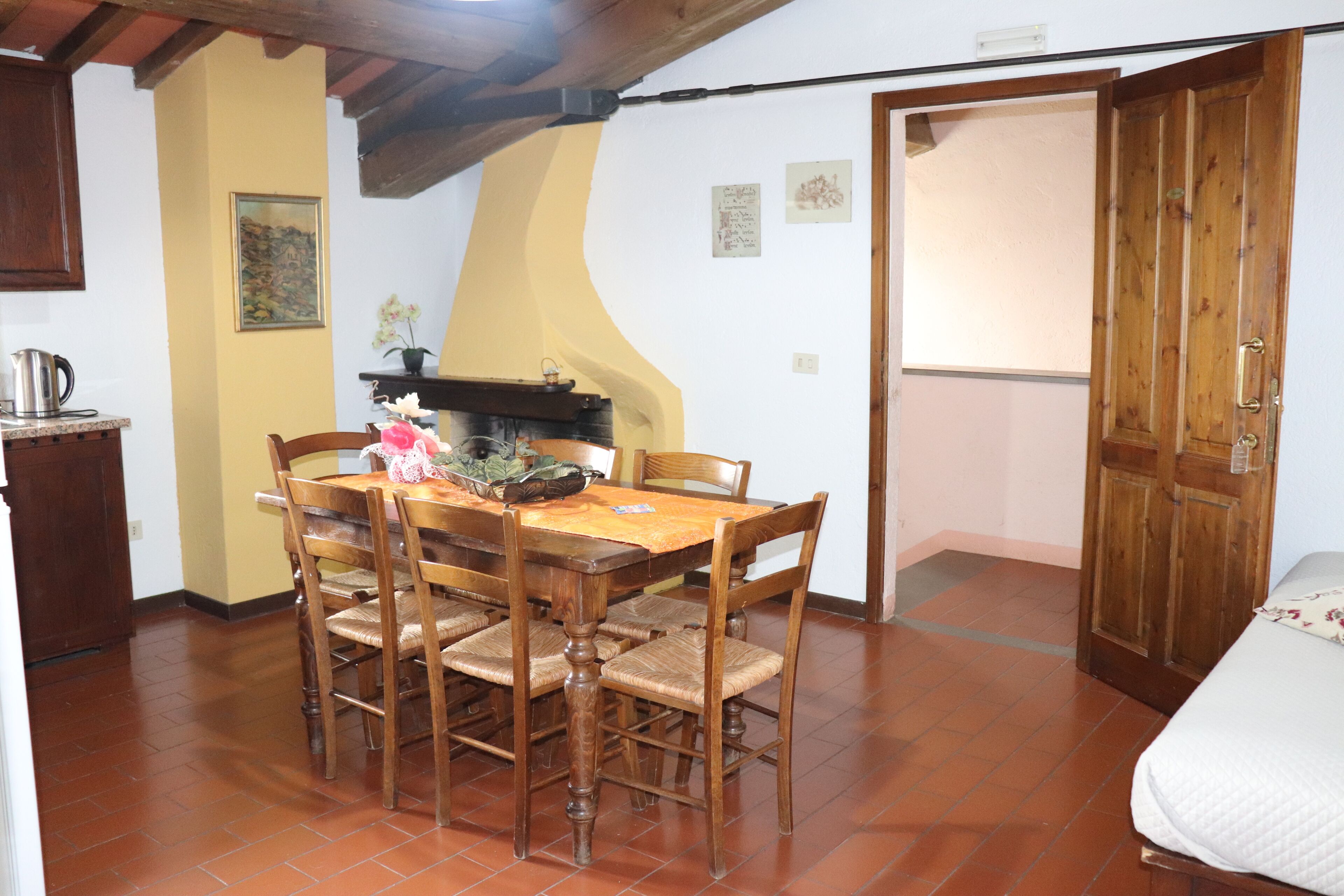 Un comedor con una mesa y sillas de madera, una zona de cocina con estufa, y una puerta que da a otra habitación.