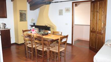 Un comedor con una mesa y sillas de madera, una zona de cocina con estufa, y una puerta que da a otra habitación.