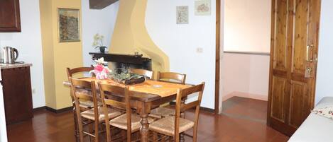 Un comedor con una mesa y sillas de madera, una zona de cocina con estufa, y una puerta que da a otra habitación.