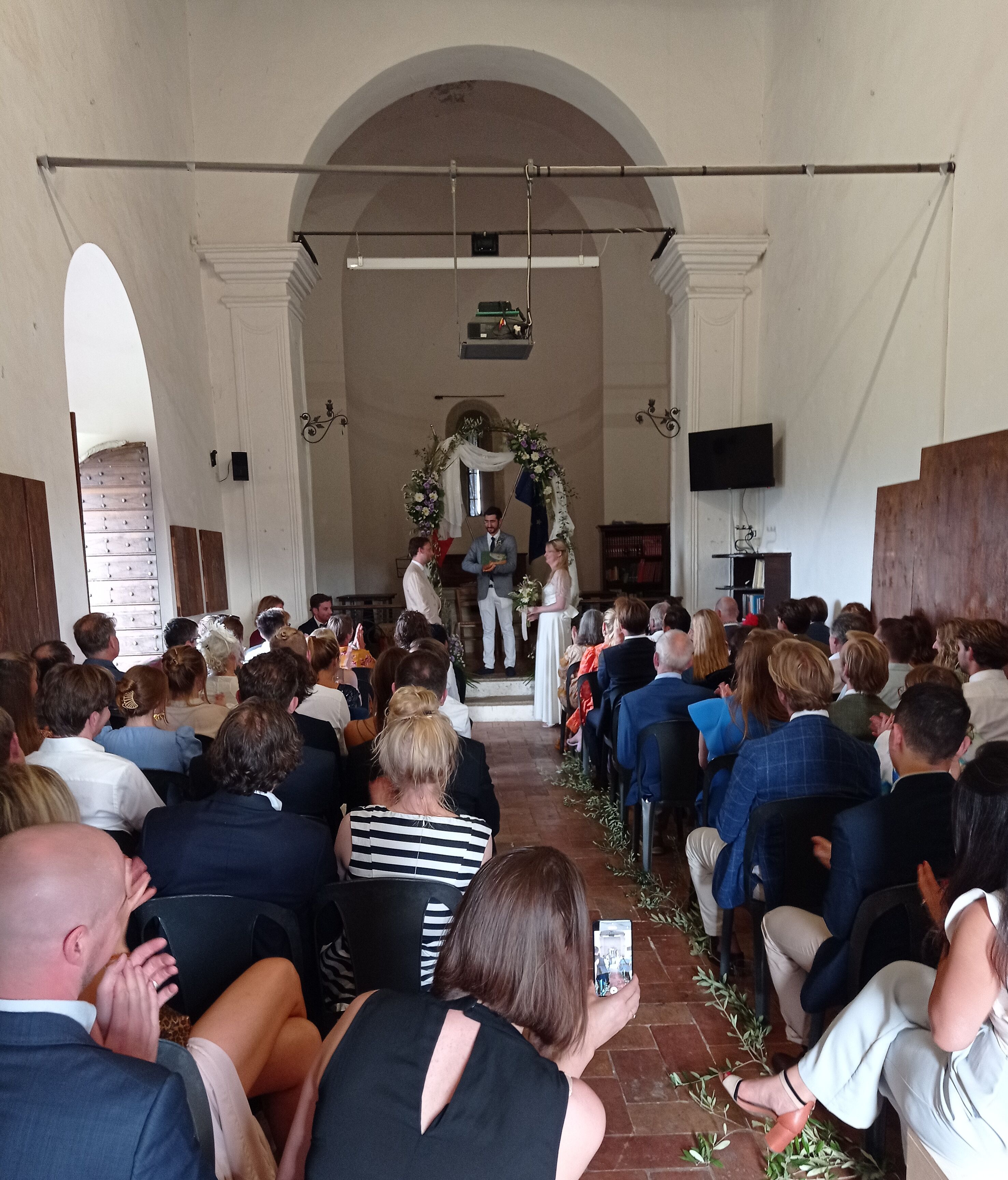 Een kerkinterieur met in rijen geplaatste banken, een centrale gang die naar een altaar leidt, en een grote gewelfde doorgang aan het einde.