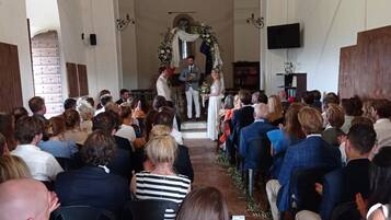 Een kerkinterieur met in rijen geplaatste banken, een centrale gang die naar een altaar leidt, en een grote gewelfde doorgang aan het einde.