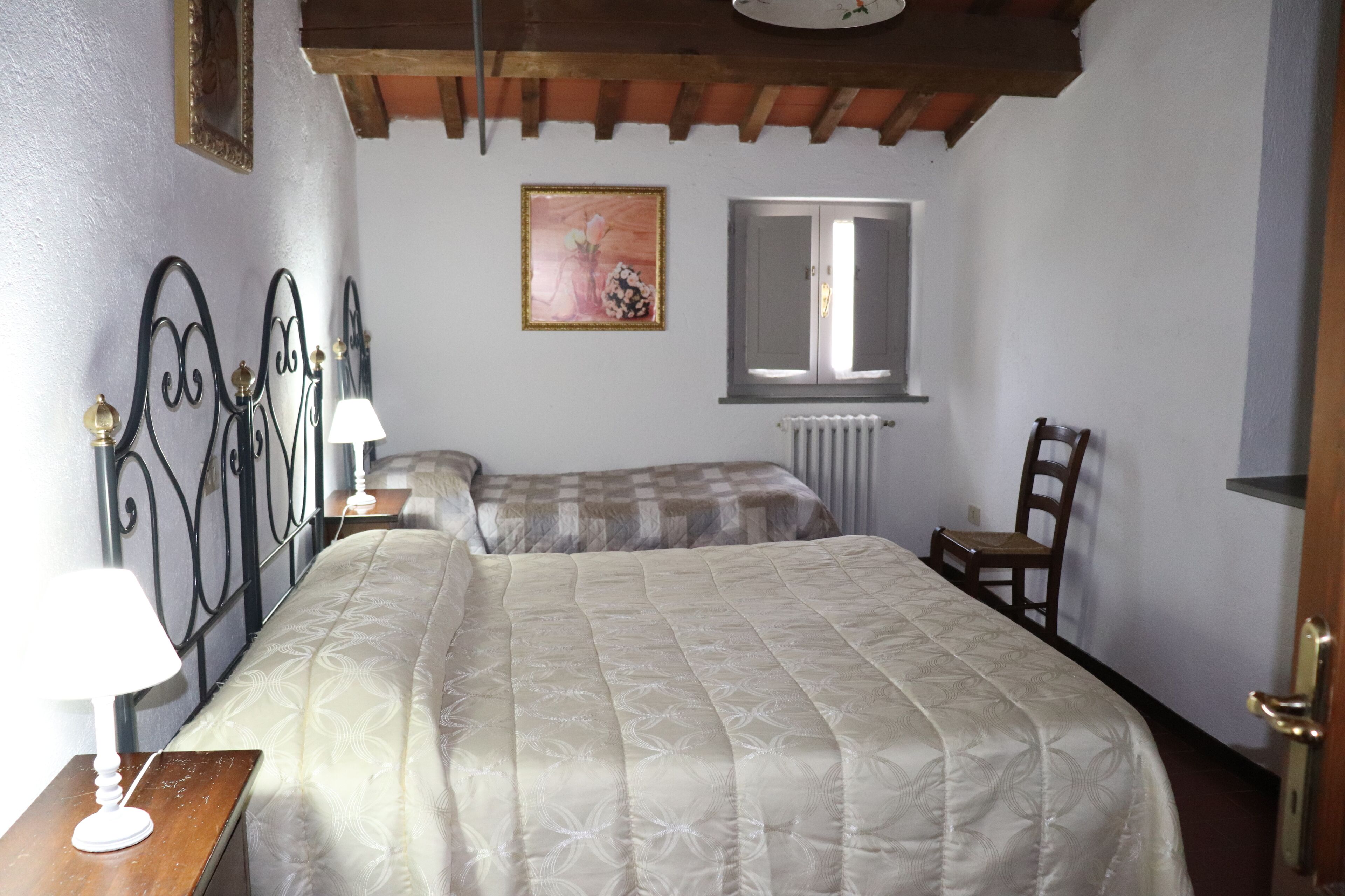 A bedroom with a bed, a bedside table with a lamp, a chair, a radiator, and a window.