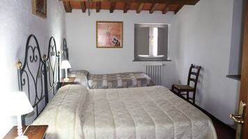 A bedroom with a bed, a bedside table with a lamp, a chair, a radiator, and a window.