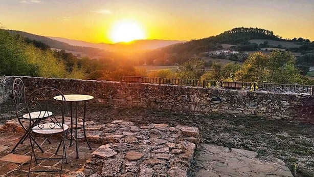 A stone patio with a metal table and chair, overlooking a valley with a sunset.
