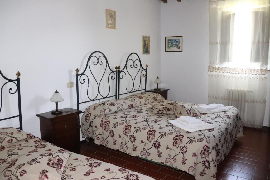 Une chambre avec deux lits, une table de chevet en bois, une lampe et une fenêtre avec des rideaux légers.