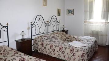 A bedroom with two beds, a wooden nightstand, a lamp, and a window with sheer curtains.