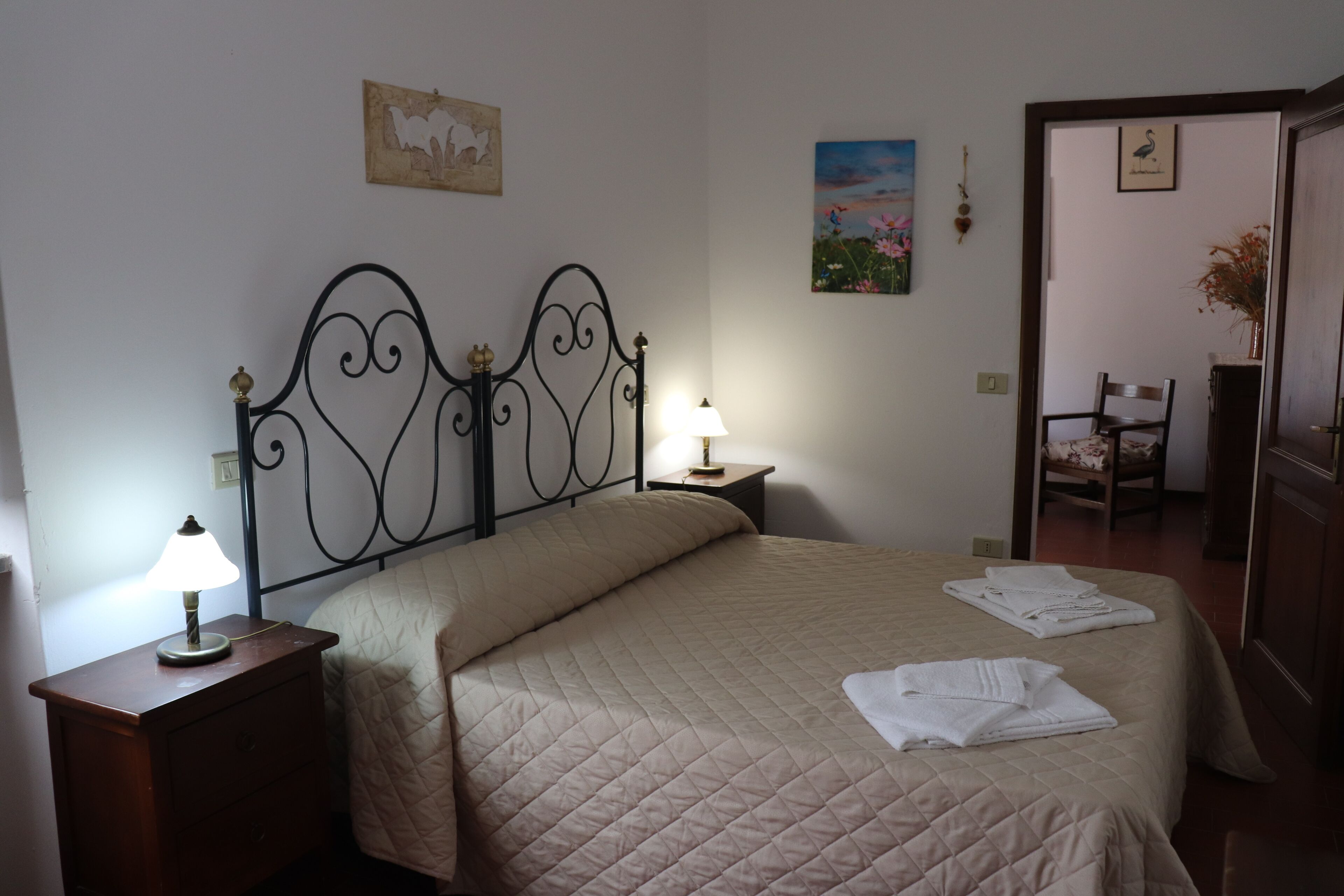 A neatly made bed with a quilted cover, a bedside lamp, and a nightstand. There is a chair and a small table in the corner.