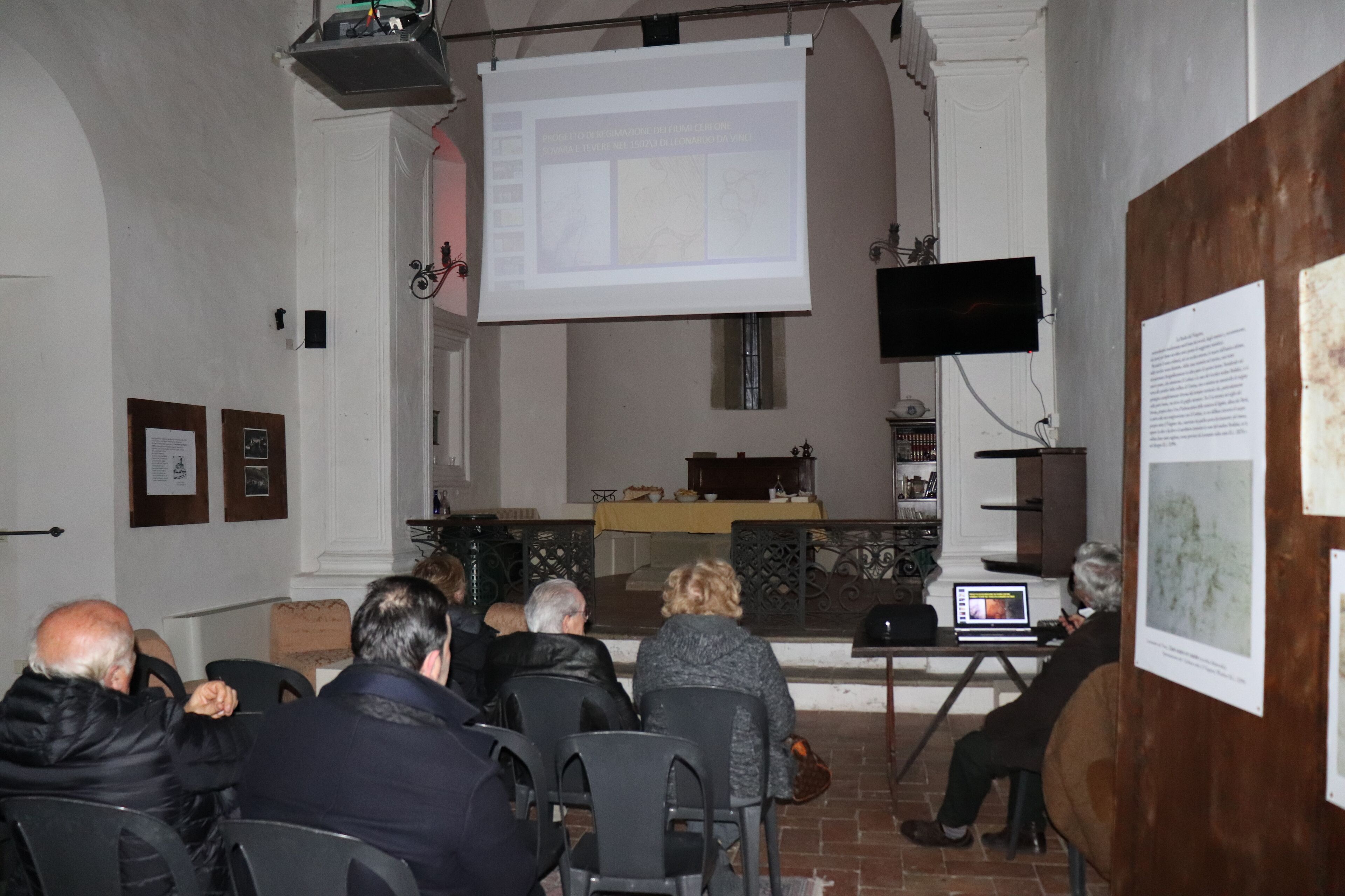 Une salle de conférence équipée d’un écran de présentation, d’un pupitre et de tables autour desquelles sont assis les participants.