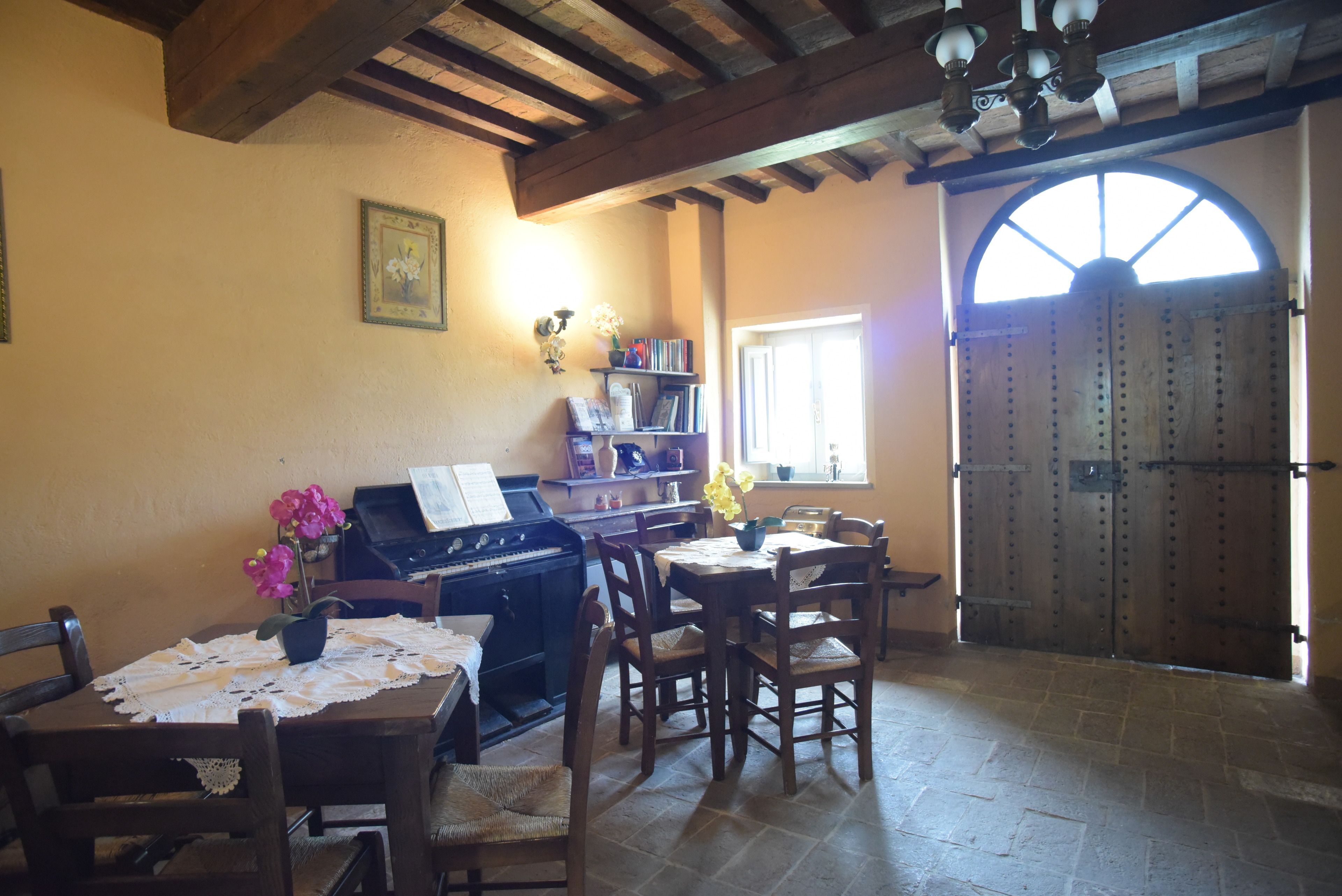 Un coin repas avec un piano, des chaises en bois, une table recouverte d’une nappe en dentelle et une bibliothèque.