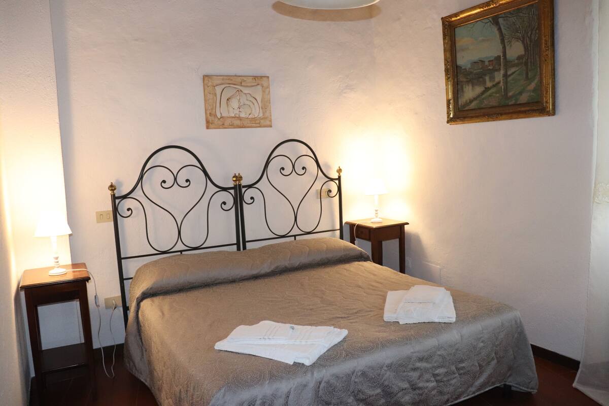 A neatly made bed with a headboard, two bedside tables with lamps, and a painting on the wall.