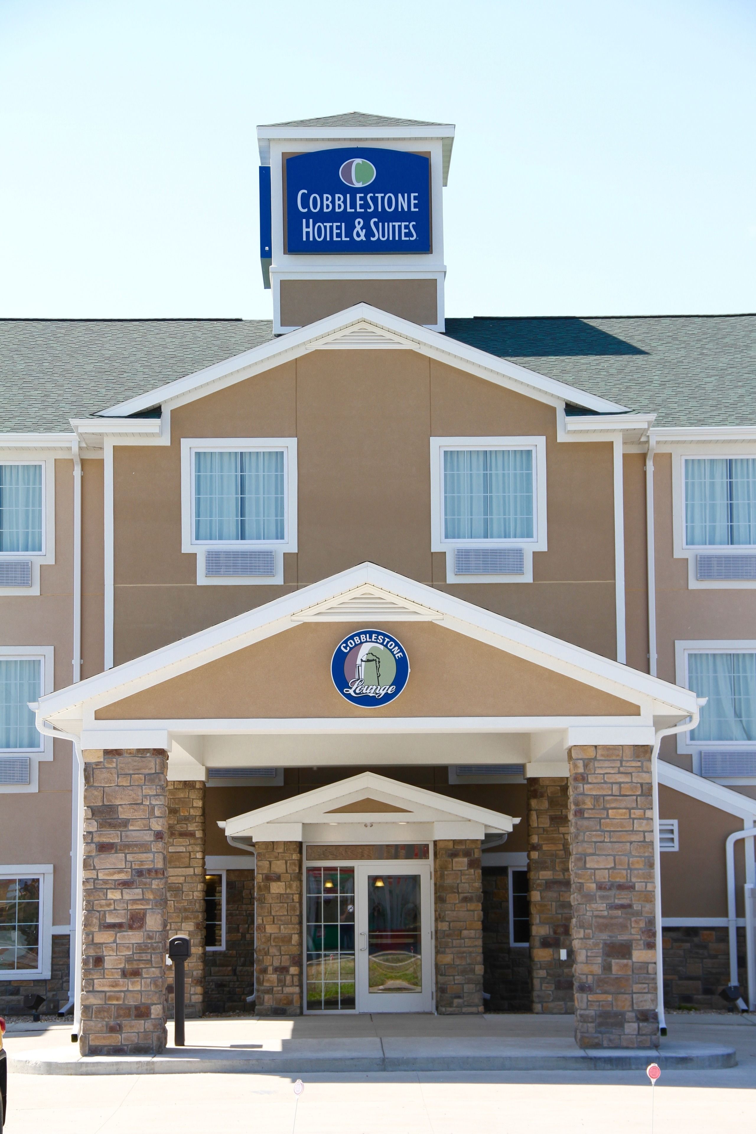 A Cobblestone Hotel & Suites with a prominent sign, a brick facade, and a covered entrance.