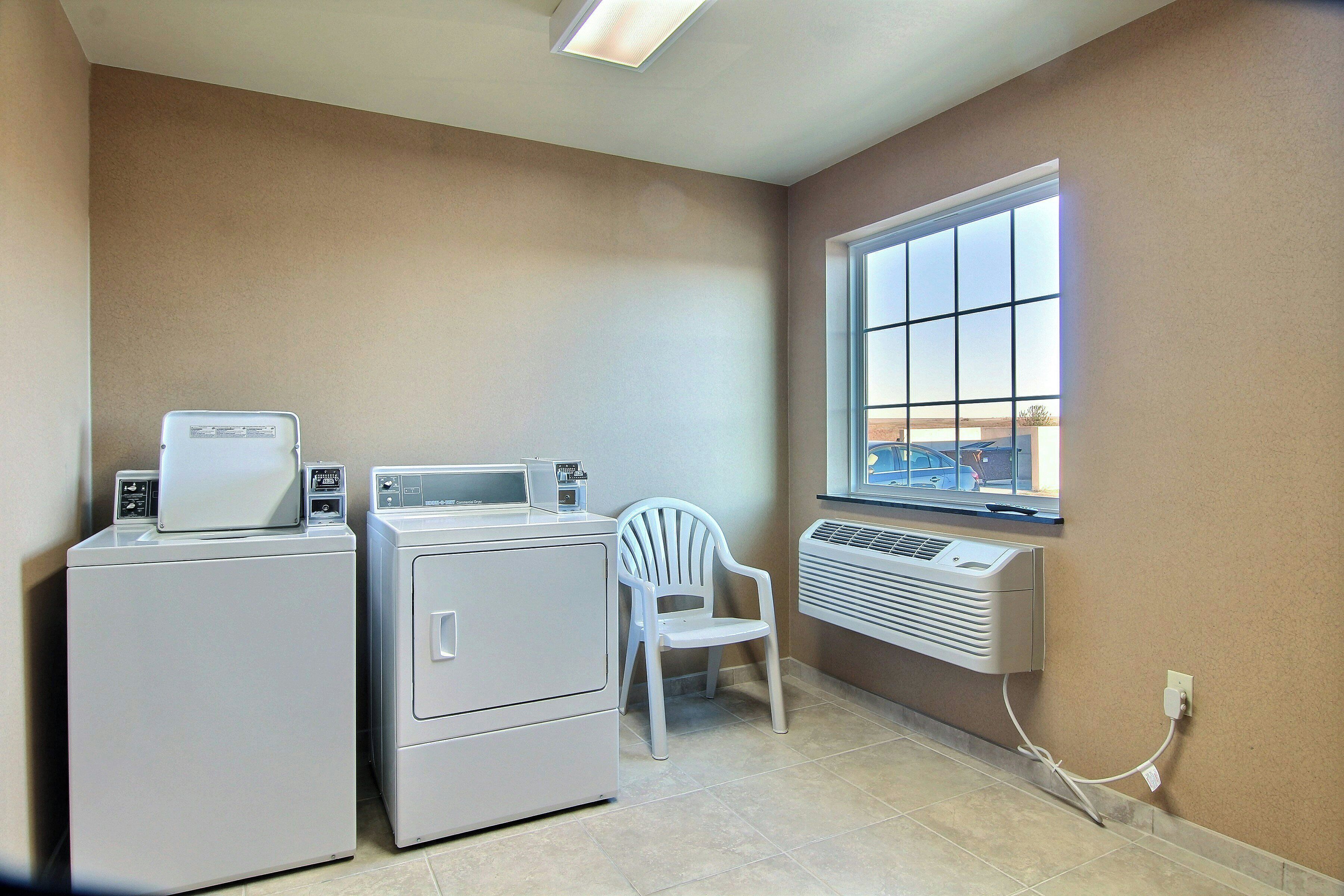 A laundry area with two washing machines, a dryer, a chair, and a window with a view.