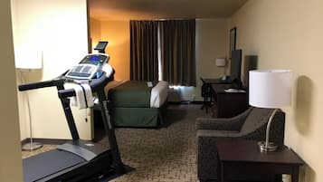 Habitación de hotel con una cinta caminadora, una cama, un escritorio, una silla y una lámpara.
