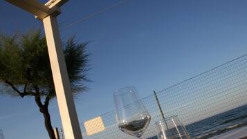 Ein Tisch mit zwei Weingläsern und freiem Blick auf das Meer durch einen Drahtzaun.