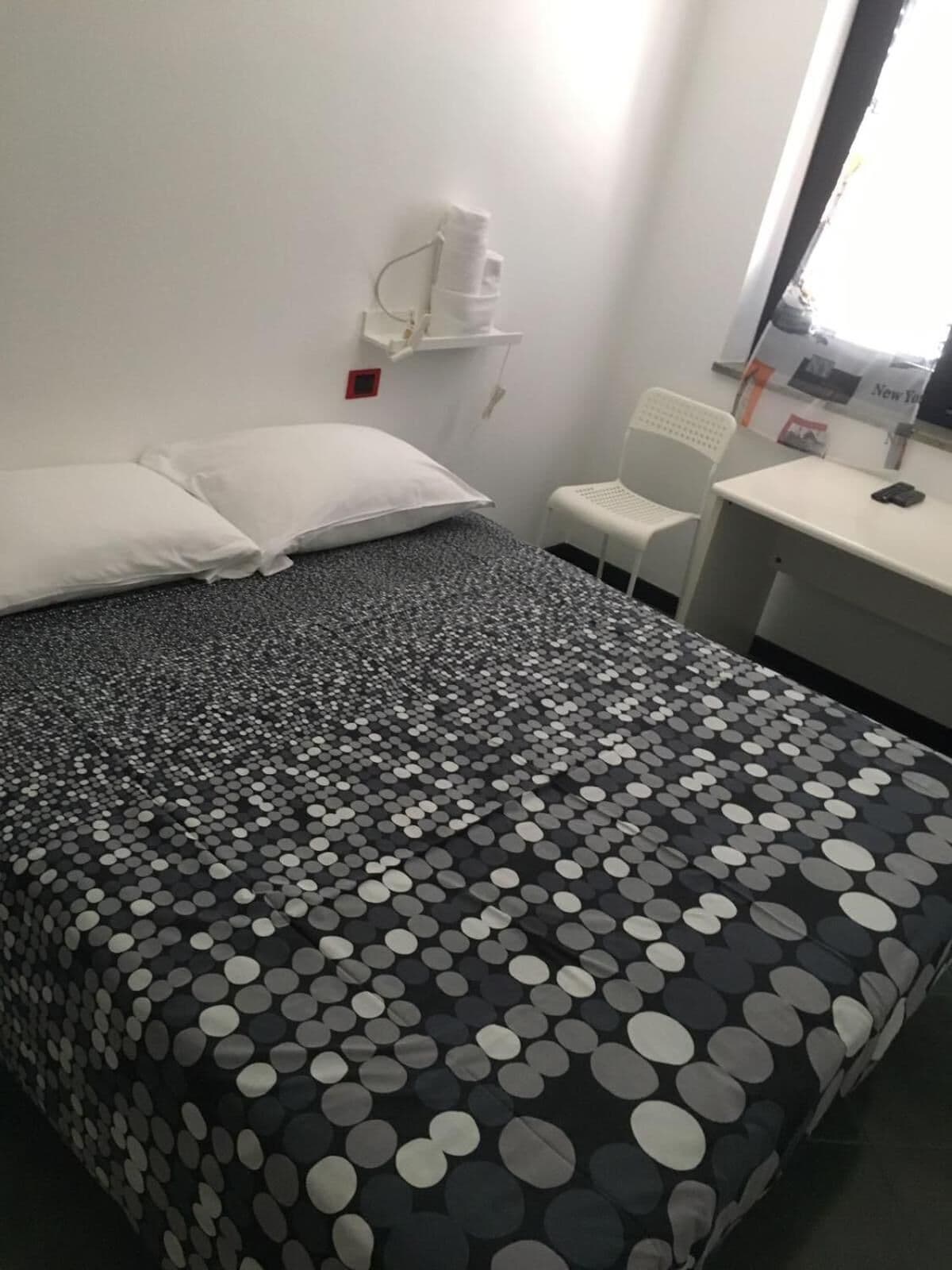 A hotel room with a bed, pillows, a chair, a desk, and a window.