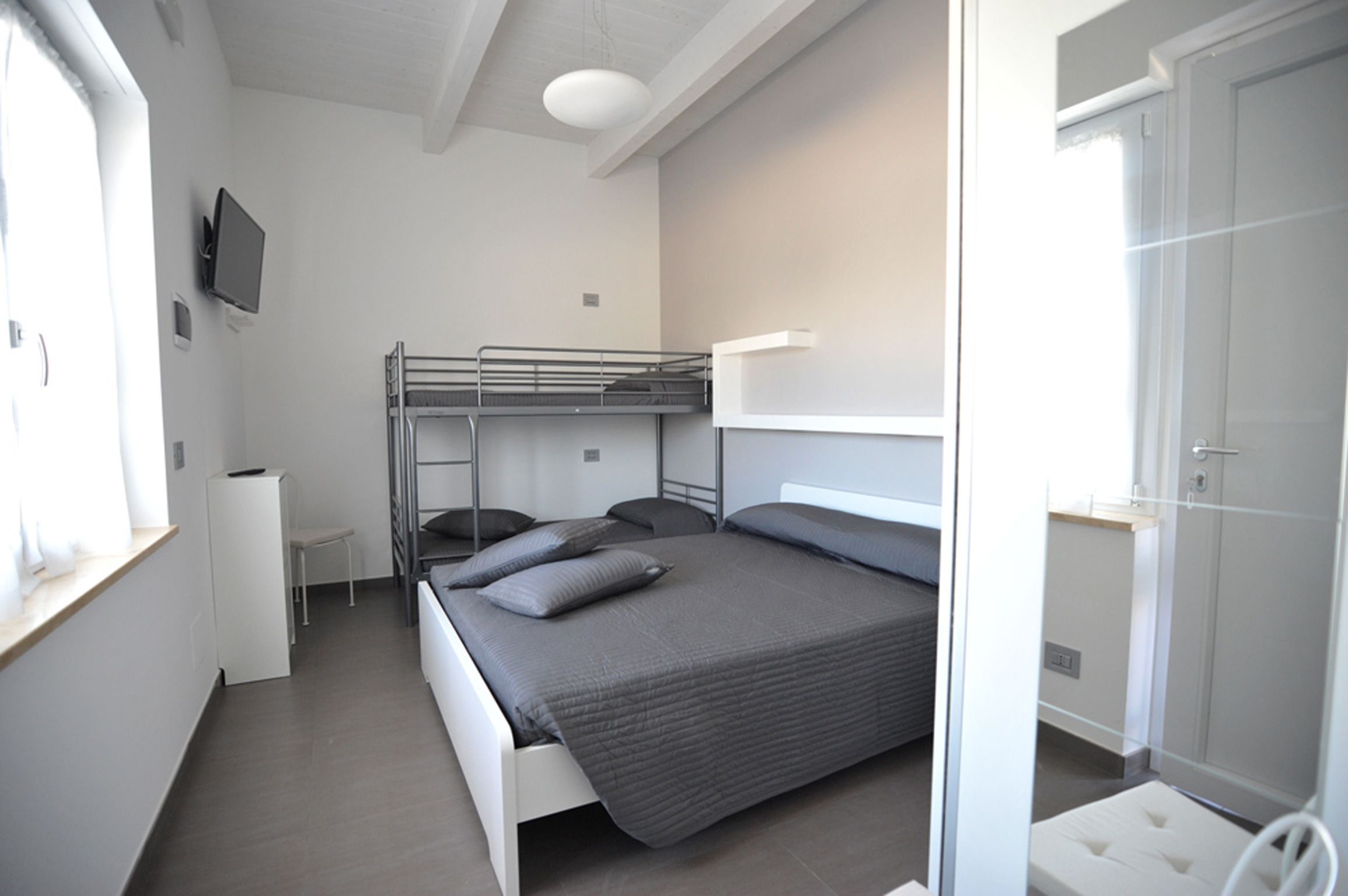Une chambre d’hôtel compacte comprenant un lit superposé, un petit bureau, une télévision et une armoire.