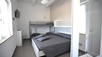 Une chambre d’hôtel compacte comprenant un lit superposé, un petit bureau, une télévision et une armoire.