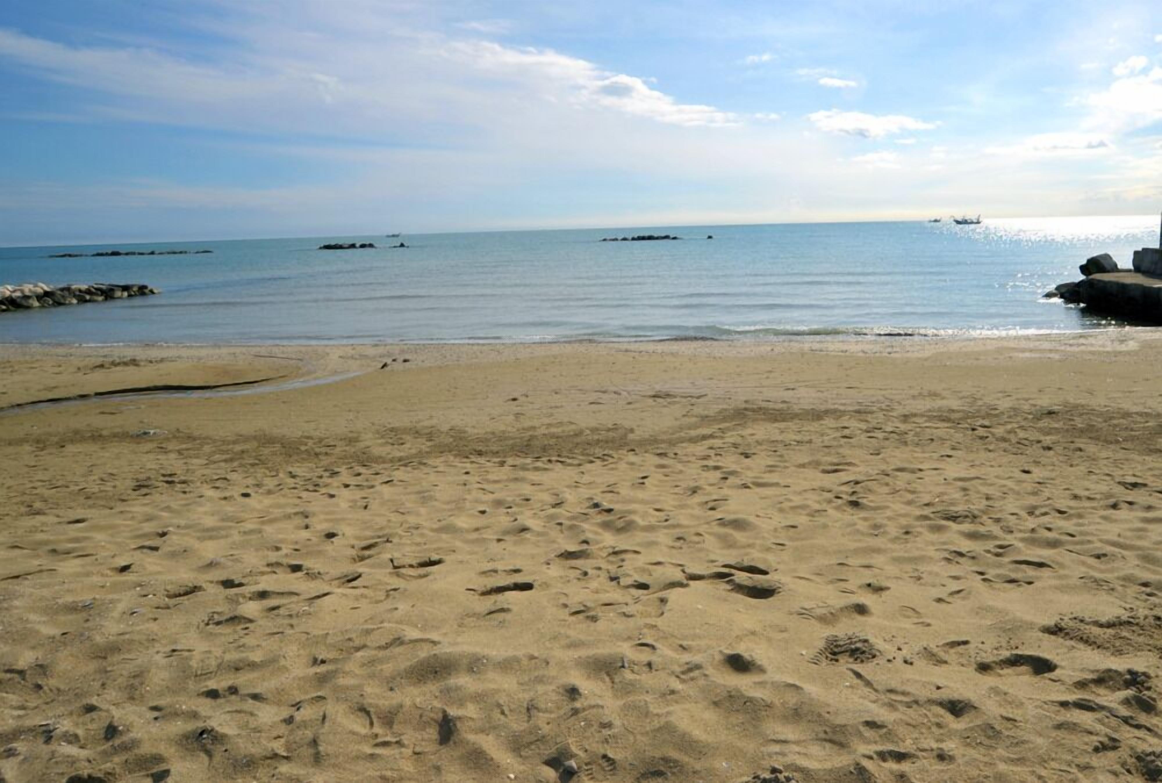 Ein sandiger Strand mit Fußspuren, ruhigem Wasser und fernen Felsen.
