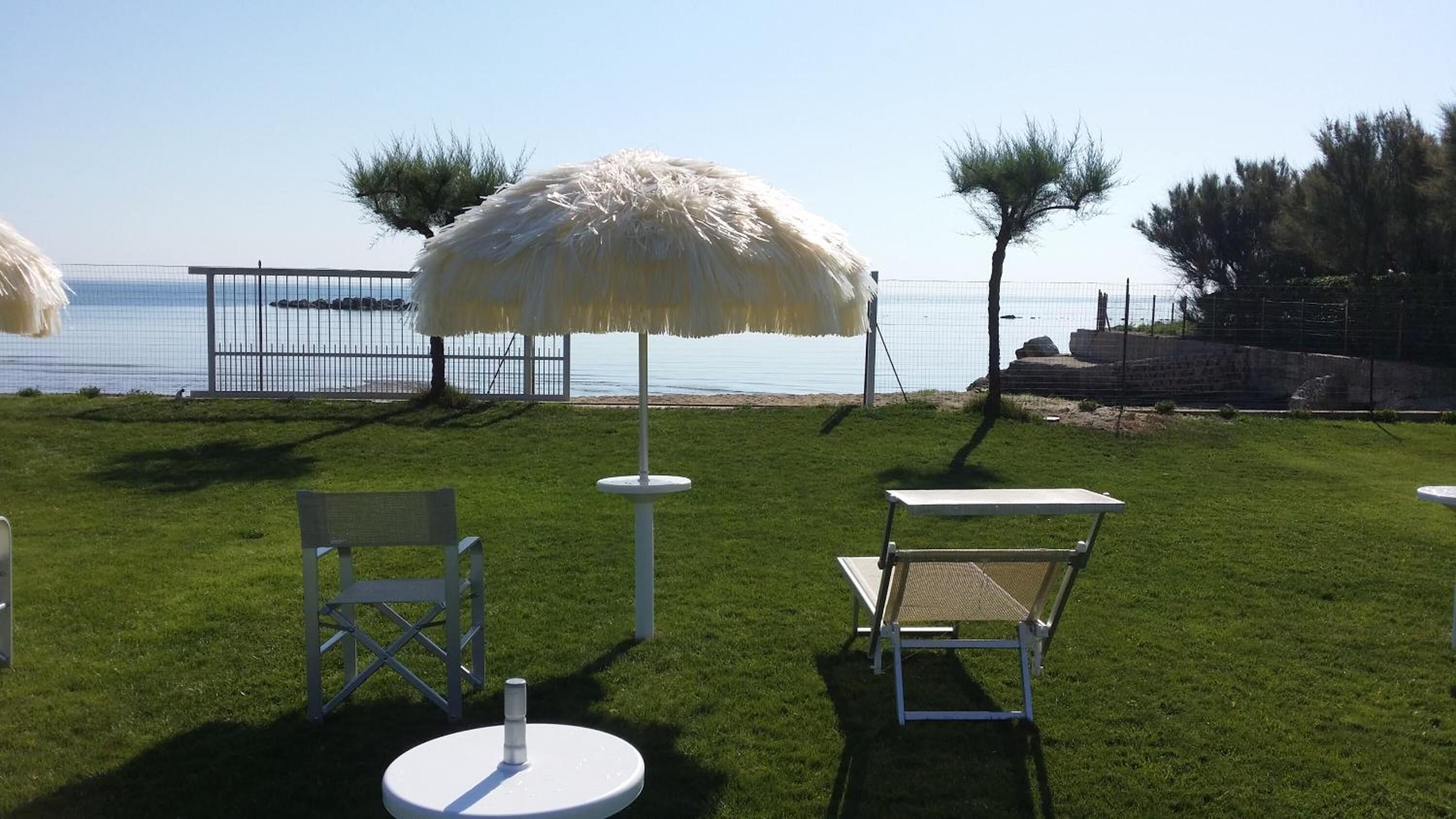 An outdoor seating area with white chairs and umbrellas, a round table, and a view of the sea.
