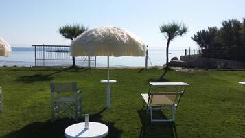 An outdoor seating area with white chairs and umbrellas, a round table, and a view of the sea.