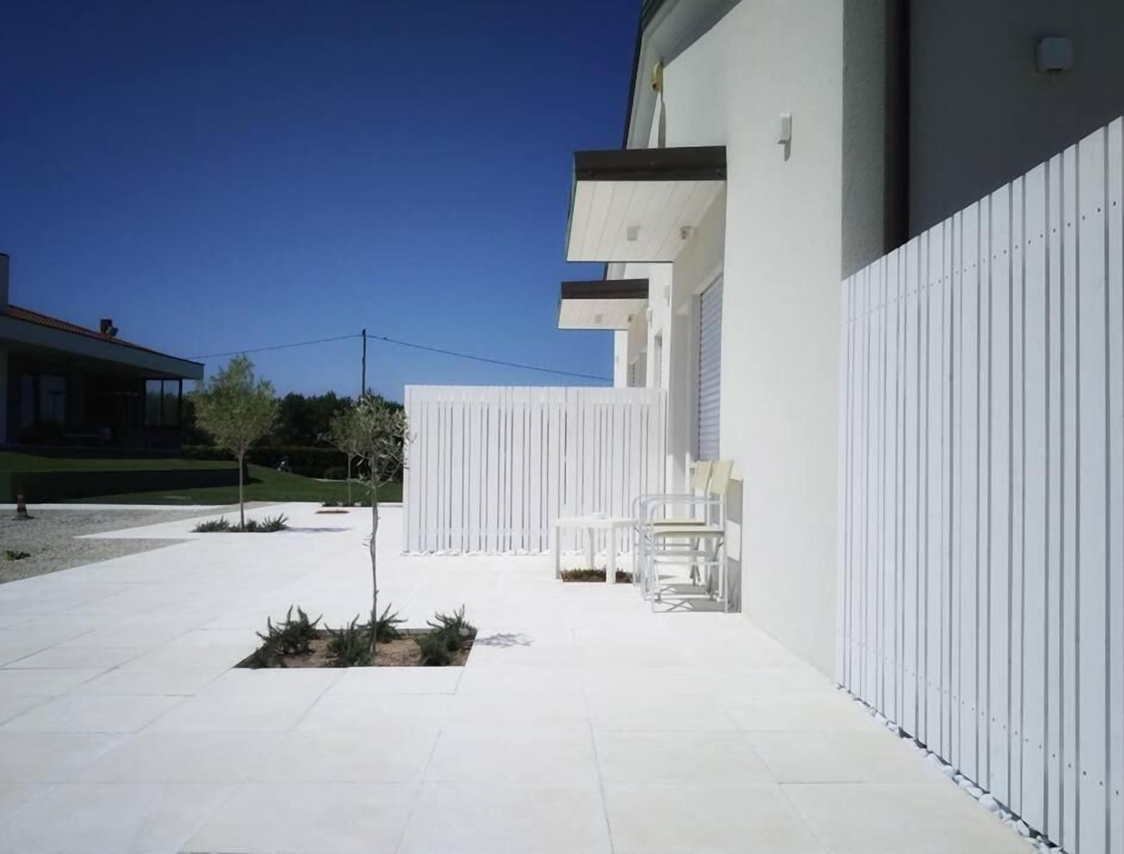 A modern building with a white exterior, a paved courtyard, and a few outdoor chairs.