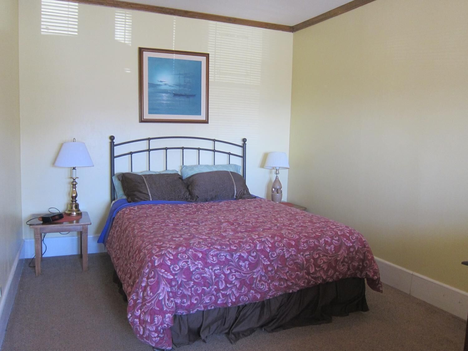 A bedroom with a bed, two bedside lamps, a framed picture on the wall, and a small table with a lamp.
