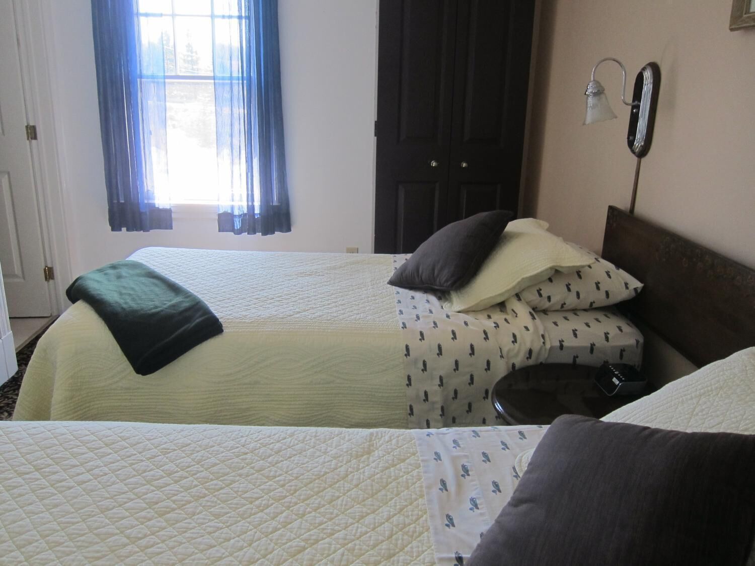 A double bed with a quilted cover, a bedside table with a lamp, and a window with curtains.