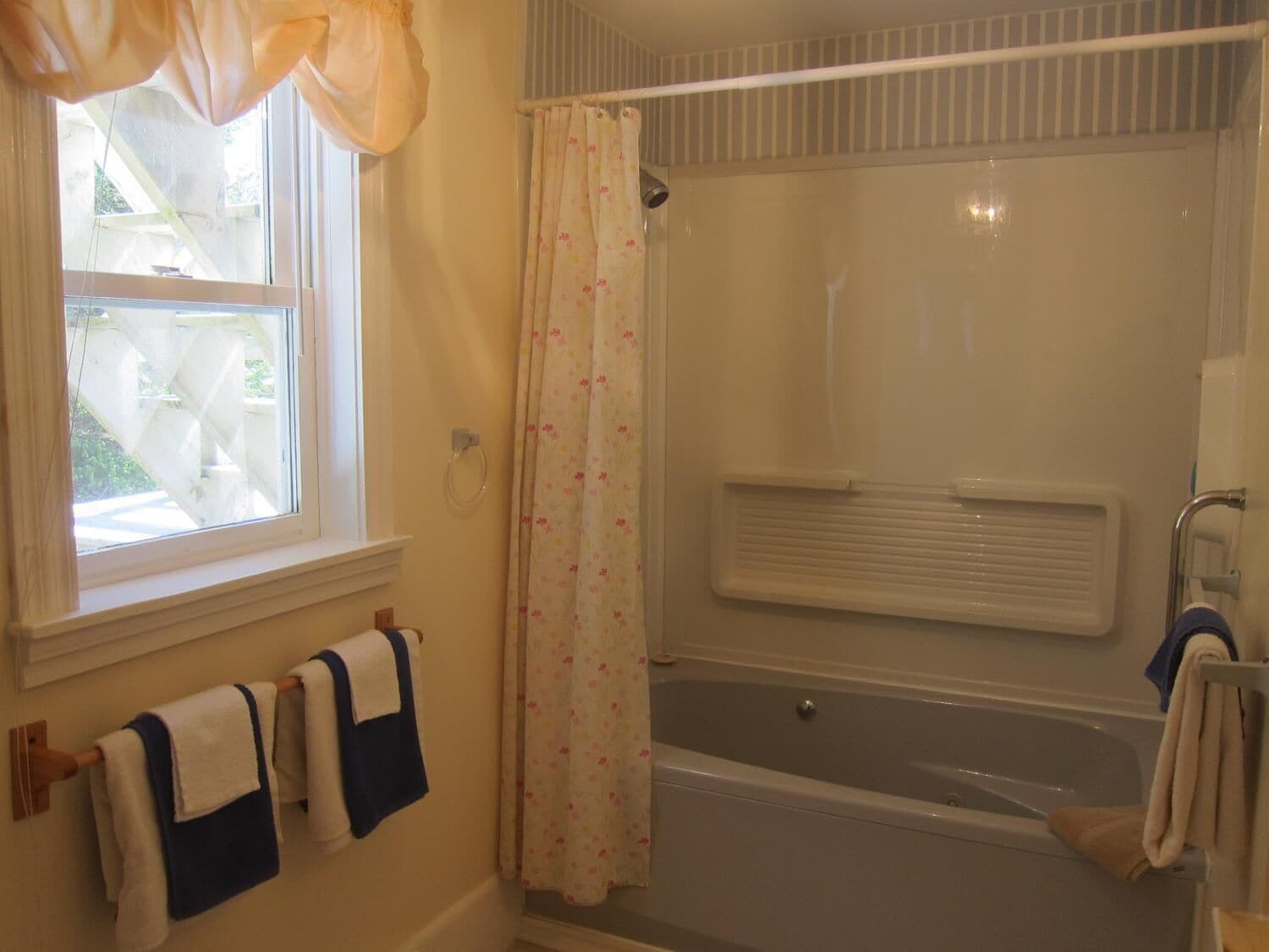 Un baño con bañera, ventana con cortinas y un perchero con toallas.