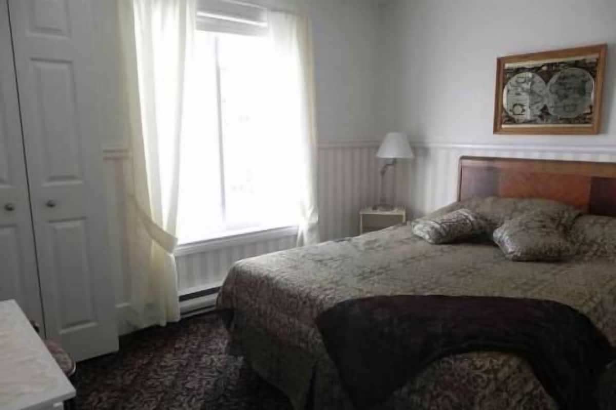 A bedroom with a bed, a nightstand, a lamp, and a window with curtains.