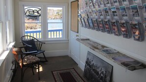 Une pièce avec une fenêtre donnant sur un quai, une chaise, un présentoir mural où sont exposées des brochures et une photographie encadrée.