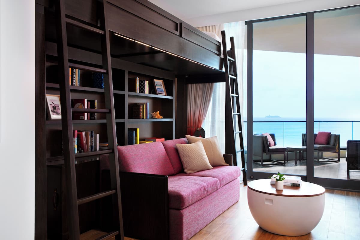A modern living room with a sofa, a bookshelf, a round coffee table, and a view of the sea through large windows.