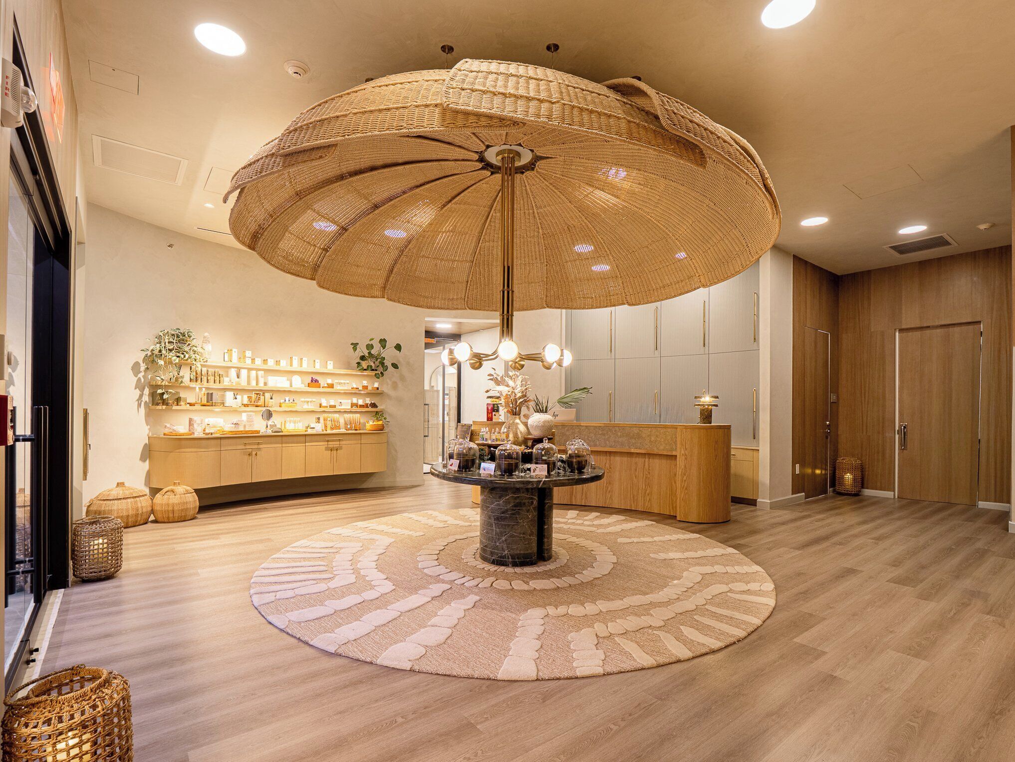 A lobby with a round table, a reception desk, and a large woven ceiling light fixture.