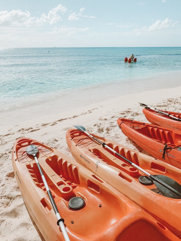 A beach with kayaks lined up on the sand, a clear blue sea, and a distant person in the water. - Kimpton Seafire Resort + Spa by IHG (Seven Mile Beach)