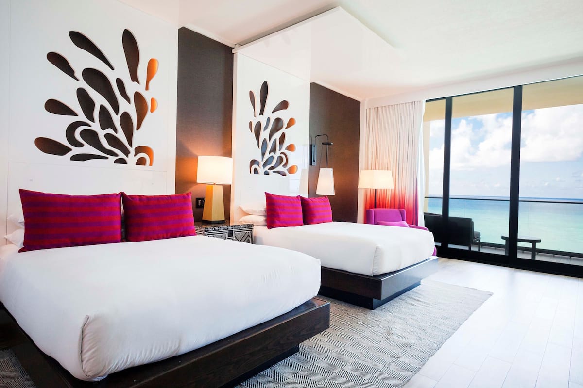 A hotel room with two beds, a large window with a view of the sea, and modern decor.