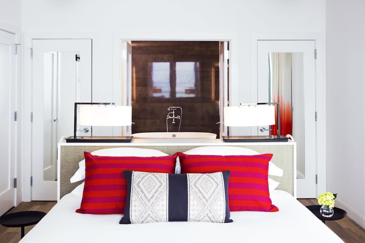 A hotel room with a large bed, two bedside tables with lamps, a large mirror, and a view of a window.