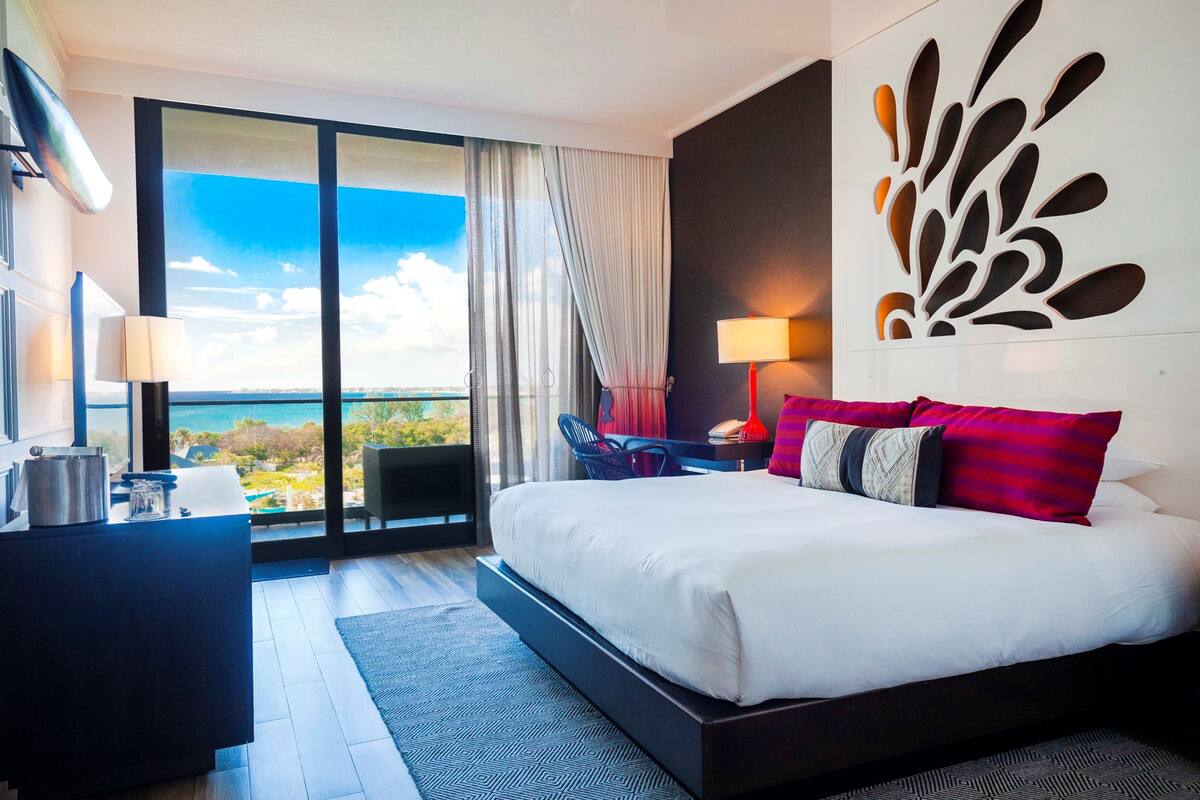 A modern hotel room with a large bed, a desk, and a view of the ocean.