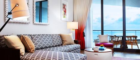 Una sala de estar moderna con un sofá estampado, una mesa de centro redonda y un ventanal con vistas al mar.
