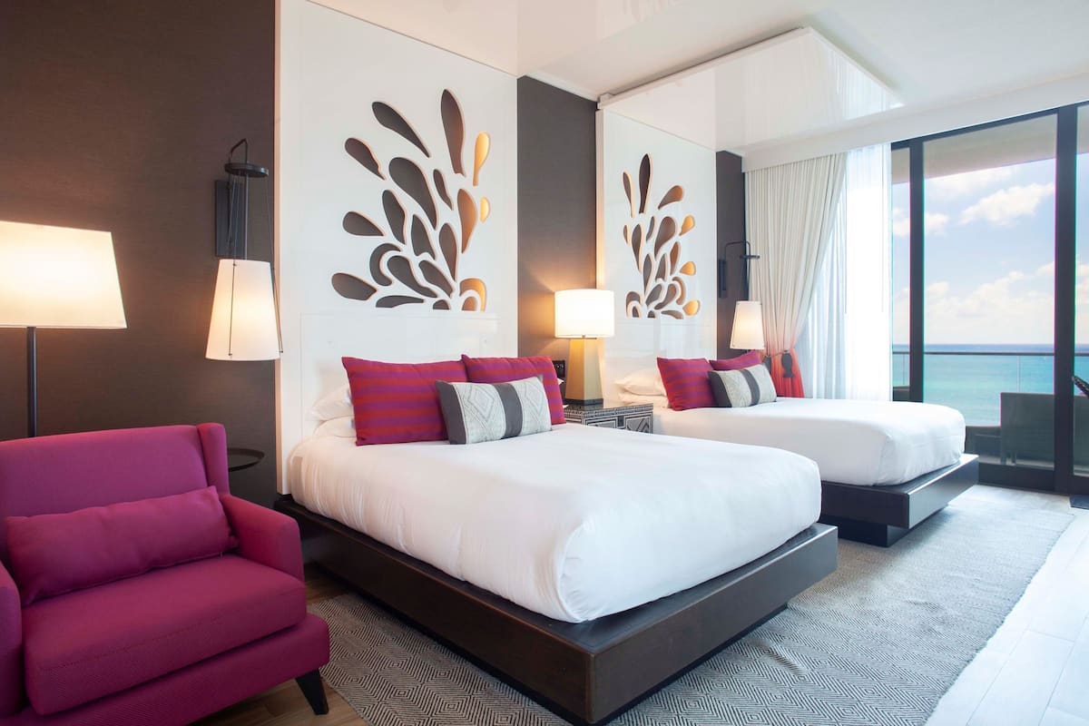 A hotel room with two beds, a red armchair, and a large window with a view.