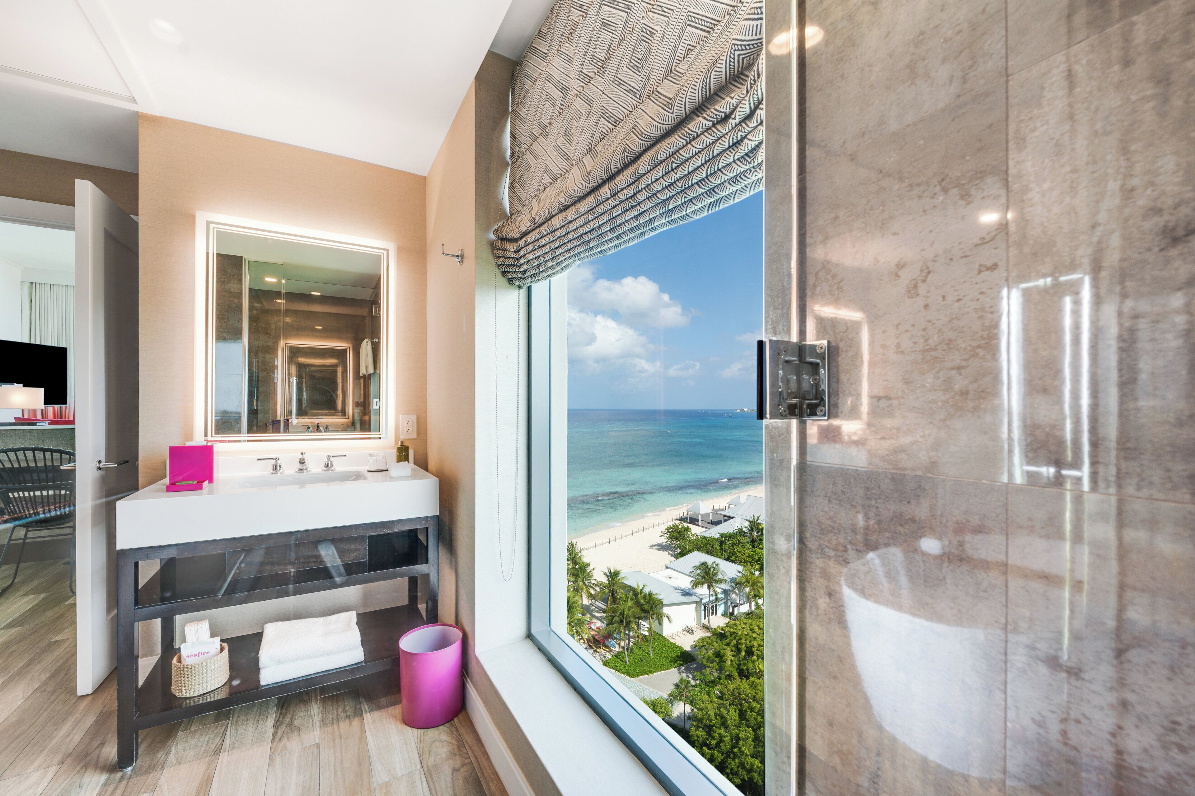 A modern bathroom with a large mirror, a sink, and a view of the beach.