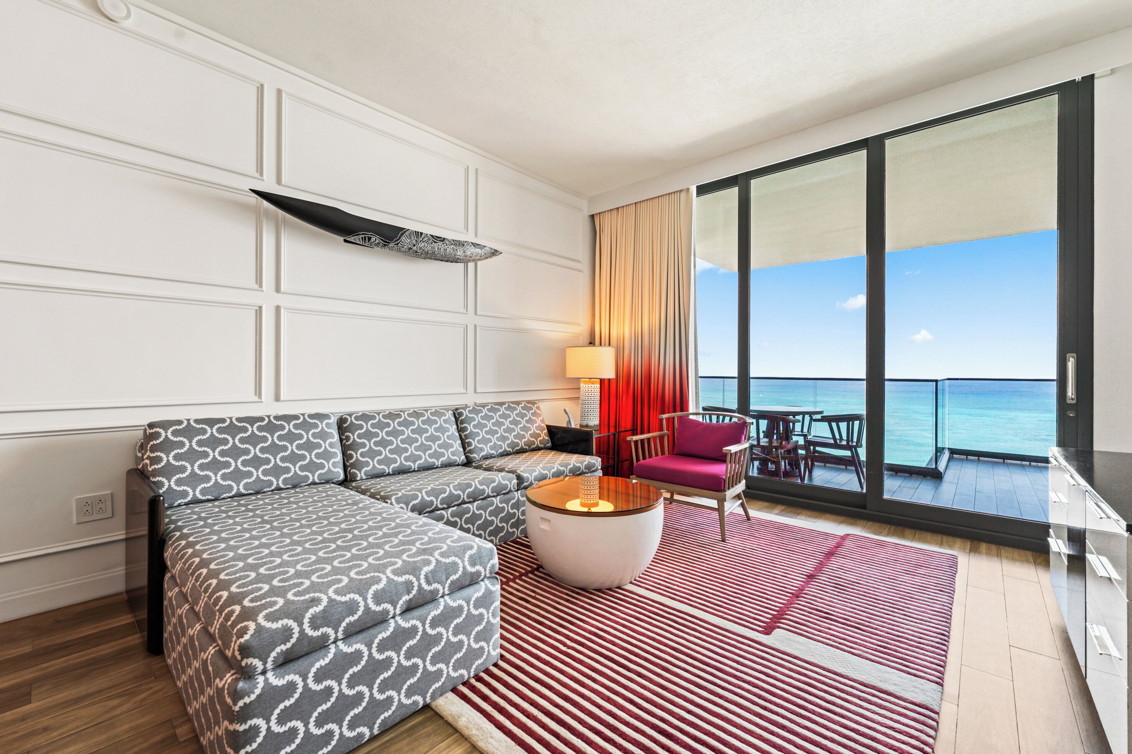 Una moderna camera d'albergo con divano, tavolino rotondo, una poltrona, una lampada e vista sul mare.