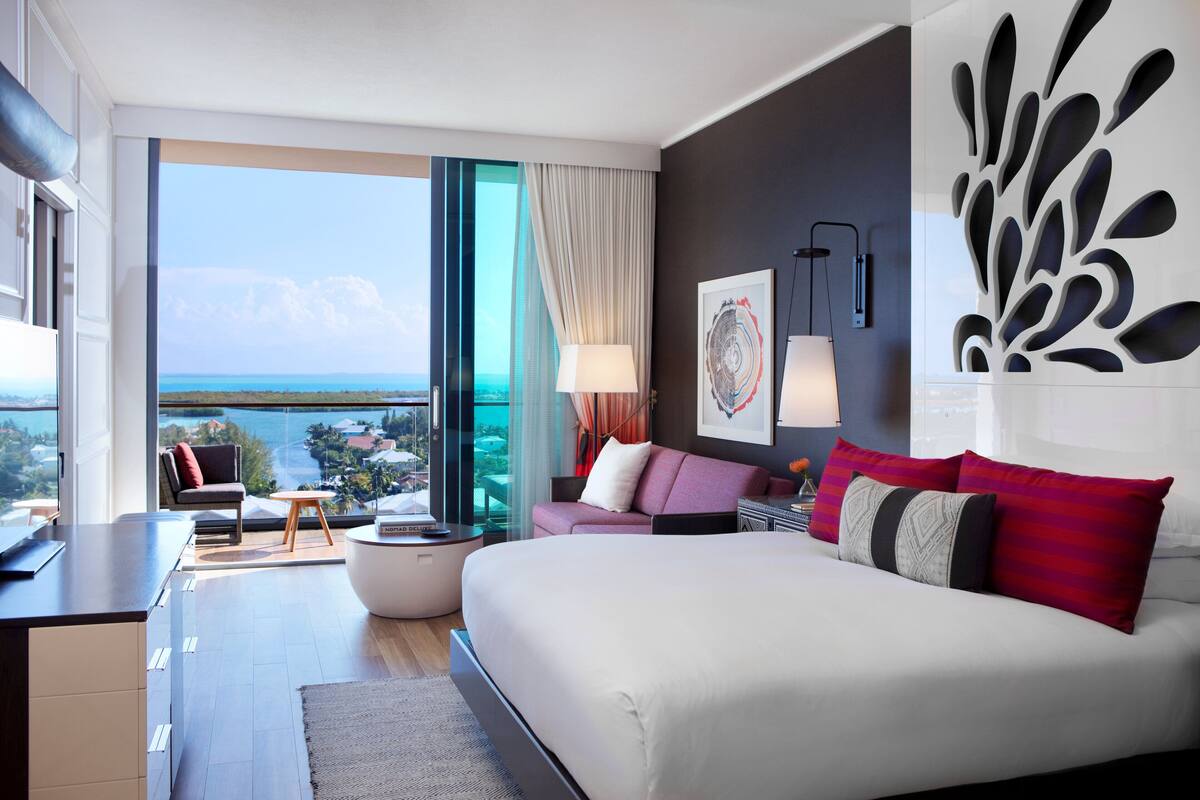 A modern hotel room with a large bed, a sofa, a dining area, and a view of the sea.