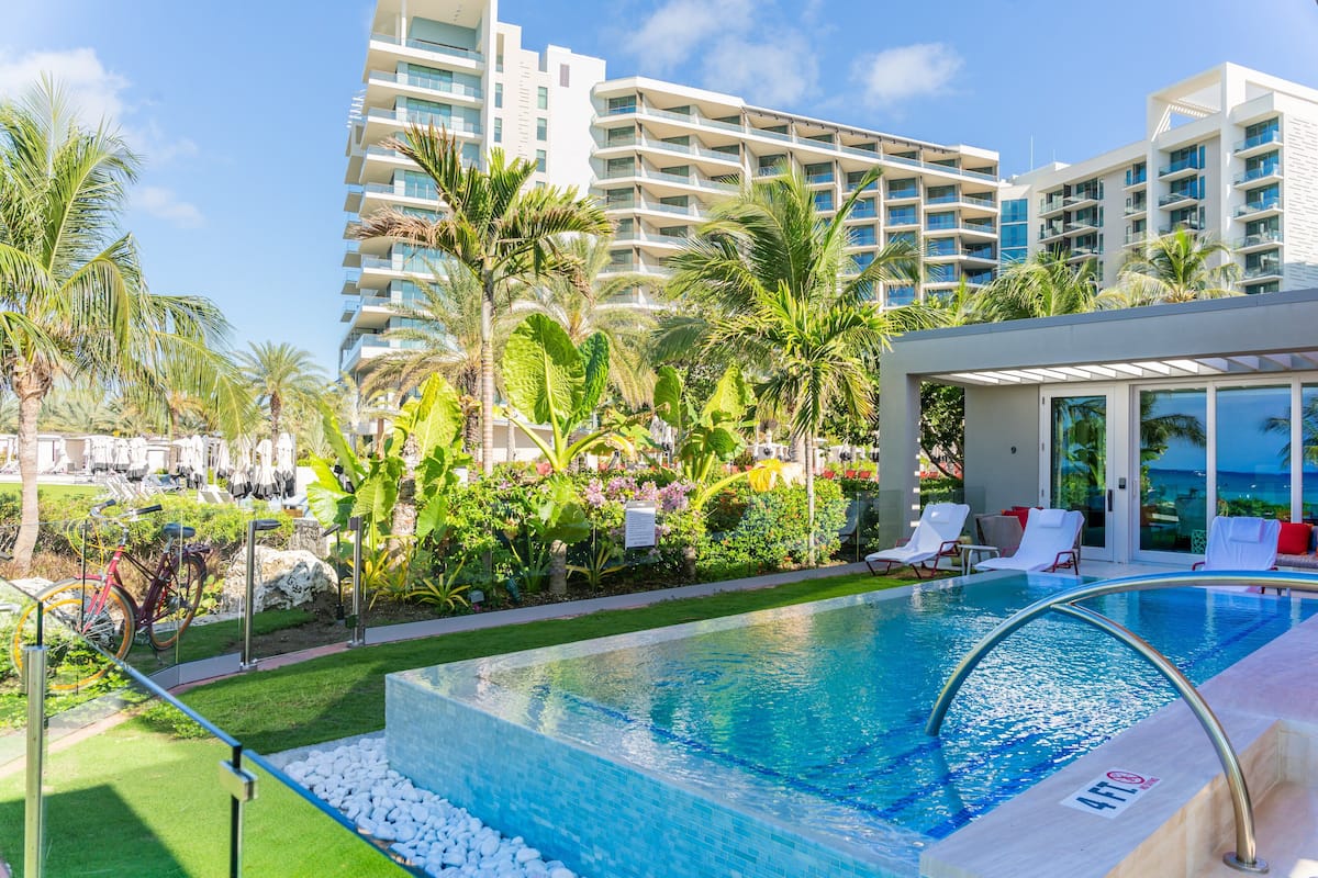 A swimming pool with a clear blue water, surrounded by white lounge chairs and palm trees.