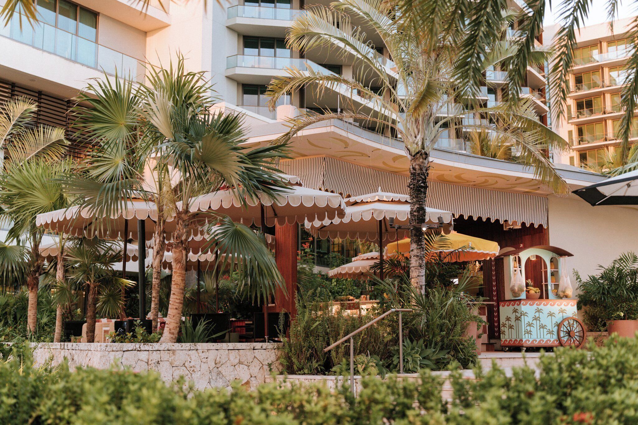 A hotel with a tropical garden, outdoor seating, and a palm tree.