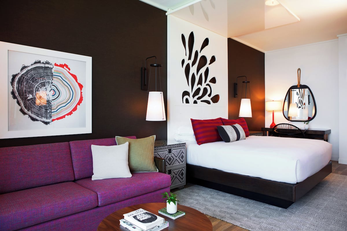 A modern hotel room with a large bed, a sofa, a coffee table, and two wall-mounted lamps.