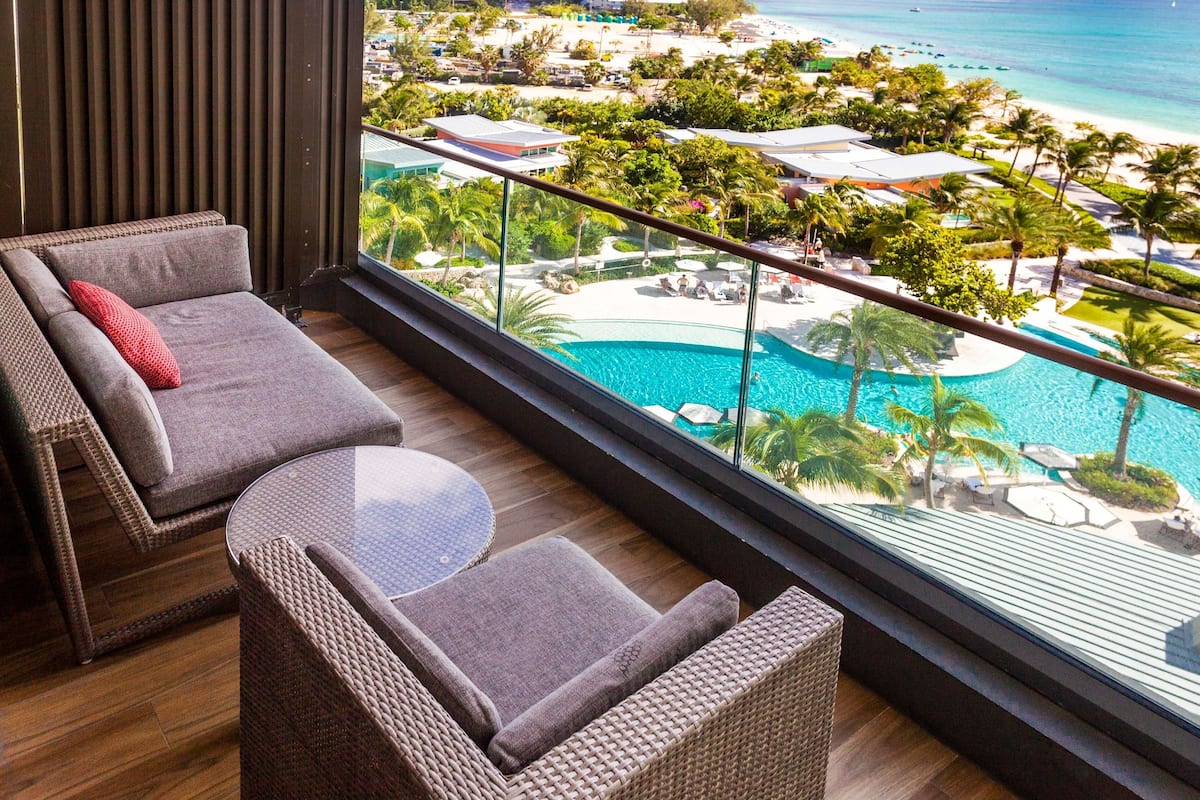 A balcony with wicker furniture overlooking a pool and beach.