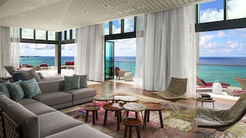 A spacious living area with a large sofa, multiple chairs, and a coffee table. The room features large windows with ocean views.