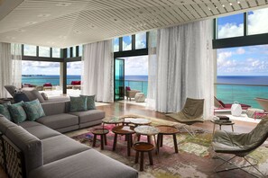 Amplia sala de estar con un sofá grande, varias sillas y una mesa de centro. La habitación cuenta con ventanas amplias y vistas al océano.