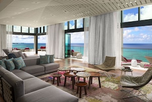 Amplia sala de estar con un sofá grande, varias sillas y una mesa de centro. La habitación cuenta con ventanas amplias y vistas al océano.